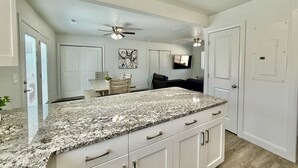 A kitchen with granite countertops, white cabinets, a ceiling fan, and a dining area with a table and chairs.