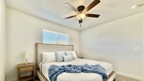 A bedroom with a bed, a nightstand, a ceiling fan, and a window with blinds.
