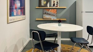 Un comedor con una mesa redonda, dos sillas, una lámpara colgante y obras de arte en las paredes.