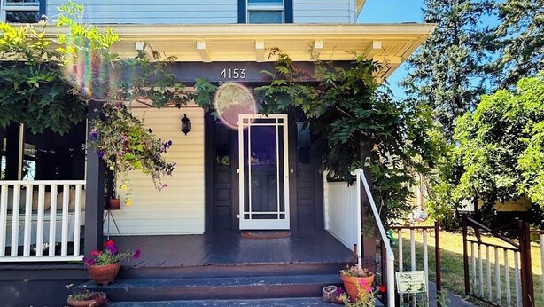Una casa de dos pisos con el número 4153 en la puerta principal, un porche cubierto con plantas en macetas y una pequeña escalera que conduce a la entrada.