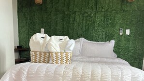 A bed with a white quilted bedspread, two woven baskets with towels, a woven rug, and a green textured wall with two wall-mounted lights. - Cozy 1-bedroom apartment in adorable Tobago with AC, WiFi (Tobago)