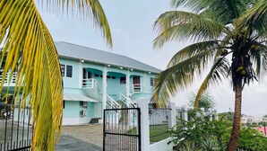 A light blue building with a staircase leading to a balcony, surrounded by palm trees and a gated entrance. - Cozy 1-bedroom apartment in adorable Tobago with AC, WiFi (Tobago)