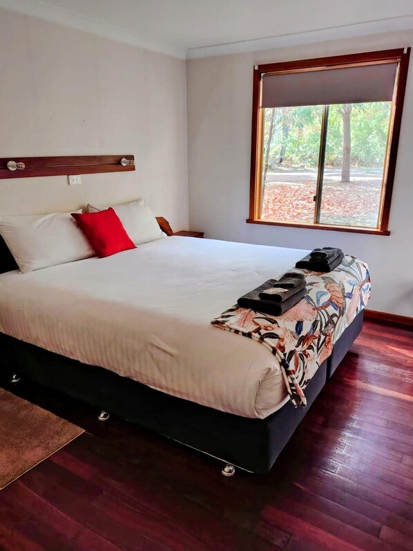 Une chambre avec un grand lit, une fenêtre donnant sur la forêt et une tête de lit en bois.