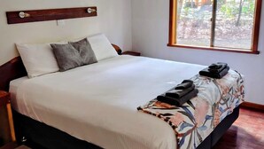 Una cama bien tendida con una colcha estampada de flores, un cabecero de madera y una ventana con vistas a árboles.