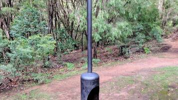 Un poteau métallique doté d’une base cylindrique et d’un fût vertical, entouré d’une zone boisée avec un sentier de terre.