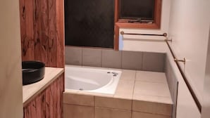 A bathroom with a bathtub, a window, and a wooden panel wall.