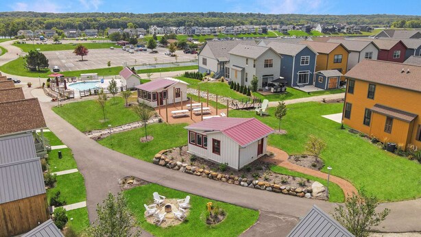 Un quartier résidentiel avec des maisons, une piscine et un petit pavillon doté d’un espace extérieur aménagé pour s’asseoir.