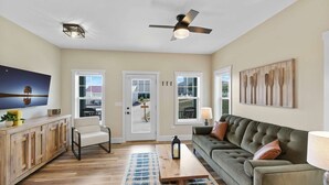 A living room with a sofa, a television, a ceiling fan, and a view through the door. - Navvy Town Neighborhood at Heritage Harbor (Ottawa)