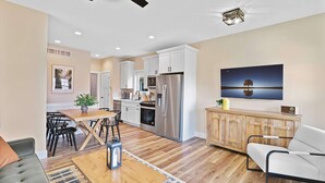 A modern kitchen with stainless steel appliances, a dining area with a wooden table and chairs, and a living room with a sofa and a TV. - Navvy Town Neighborhood at Heritage Harbor (Ottawa)