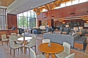 A spacious lobby with multiple seating areas, including round tables and sofas, and large windows offering views of the outdoors.
