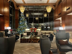 A lobby with a large Christmas tree, leather chairs, a wooden reception desk, and chandeliers.