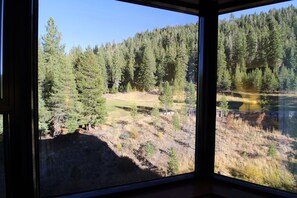 A room with a large window offering a view of a forested area with a lake.