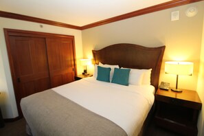 A hotel room with a large bed, two bedside tables with lamps, a wooden wardrobe, and a wall-mounted light fixture.