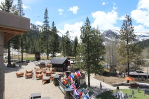 A patio area with outdoor seating and flags, surrounded by trees and a mountain view.