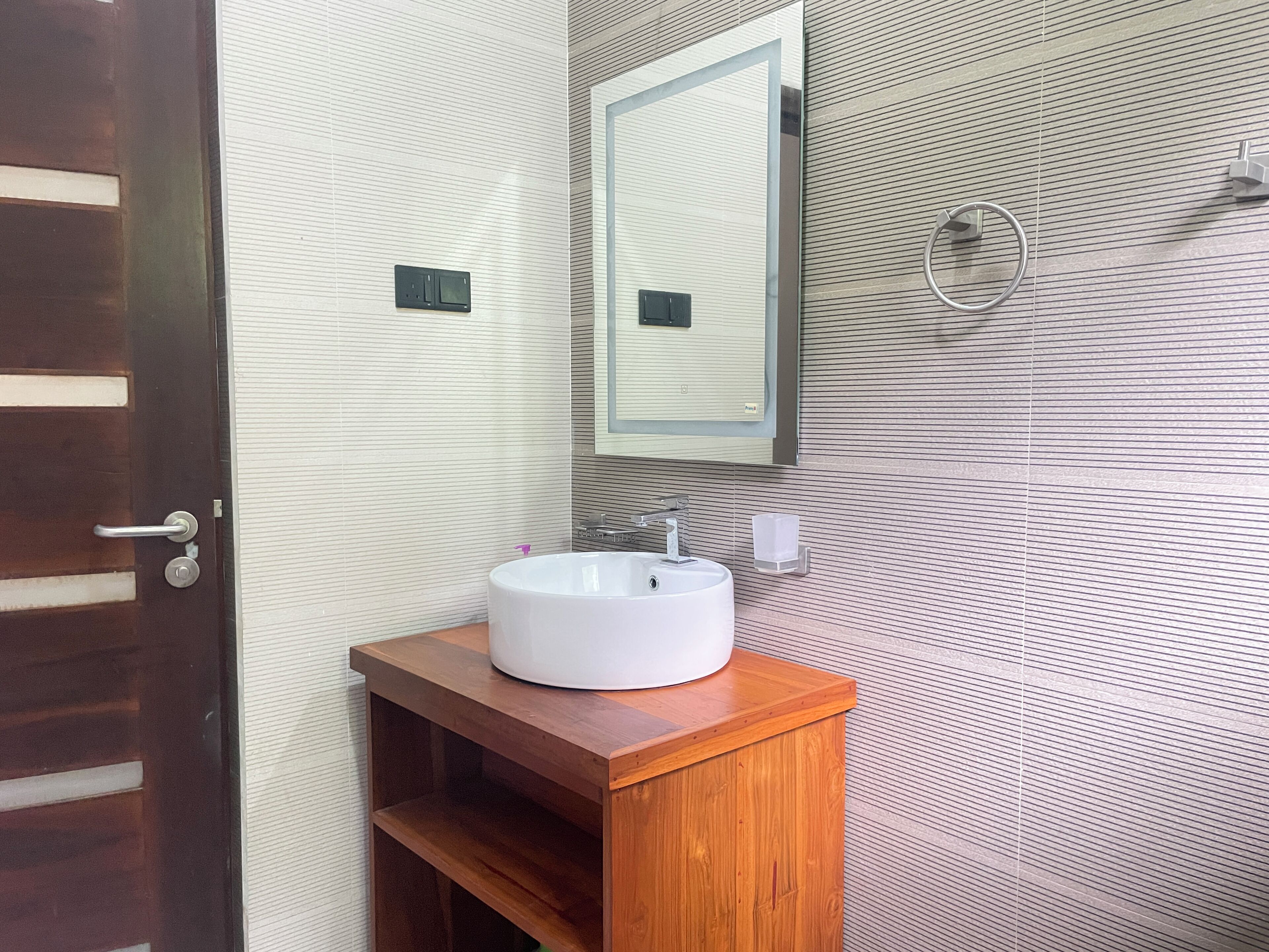 A bathroom with a wooden vanity, a white sink, a mirror, and a towel ring on the wall.