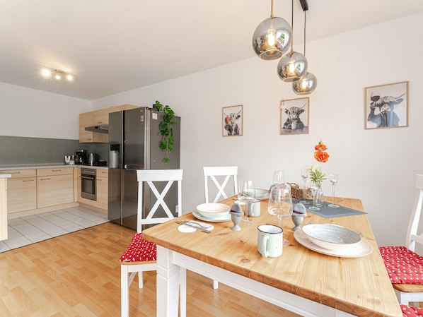 A modern kitchen with a dining area, featuring a wooden table, white chairs, and a refrigerator. - Light-flooded vacation apartment Felix - your Allgäu dream in a quiet idyll (Weitnau)