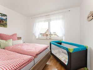 A bedroom with a bed, a crib, a window with curtains, and a wall-mounted picture. - Light-flooded vacation apartment Felix - your Allgäu dream in a quiet idyll (Weitnau)