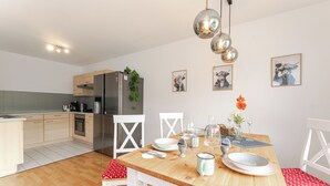 Une cuisine moderne avec des meubles en bois, un réfrigérateur en acier inoxydable et une table à manger pour quatre personnes.