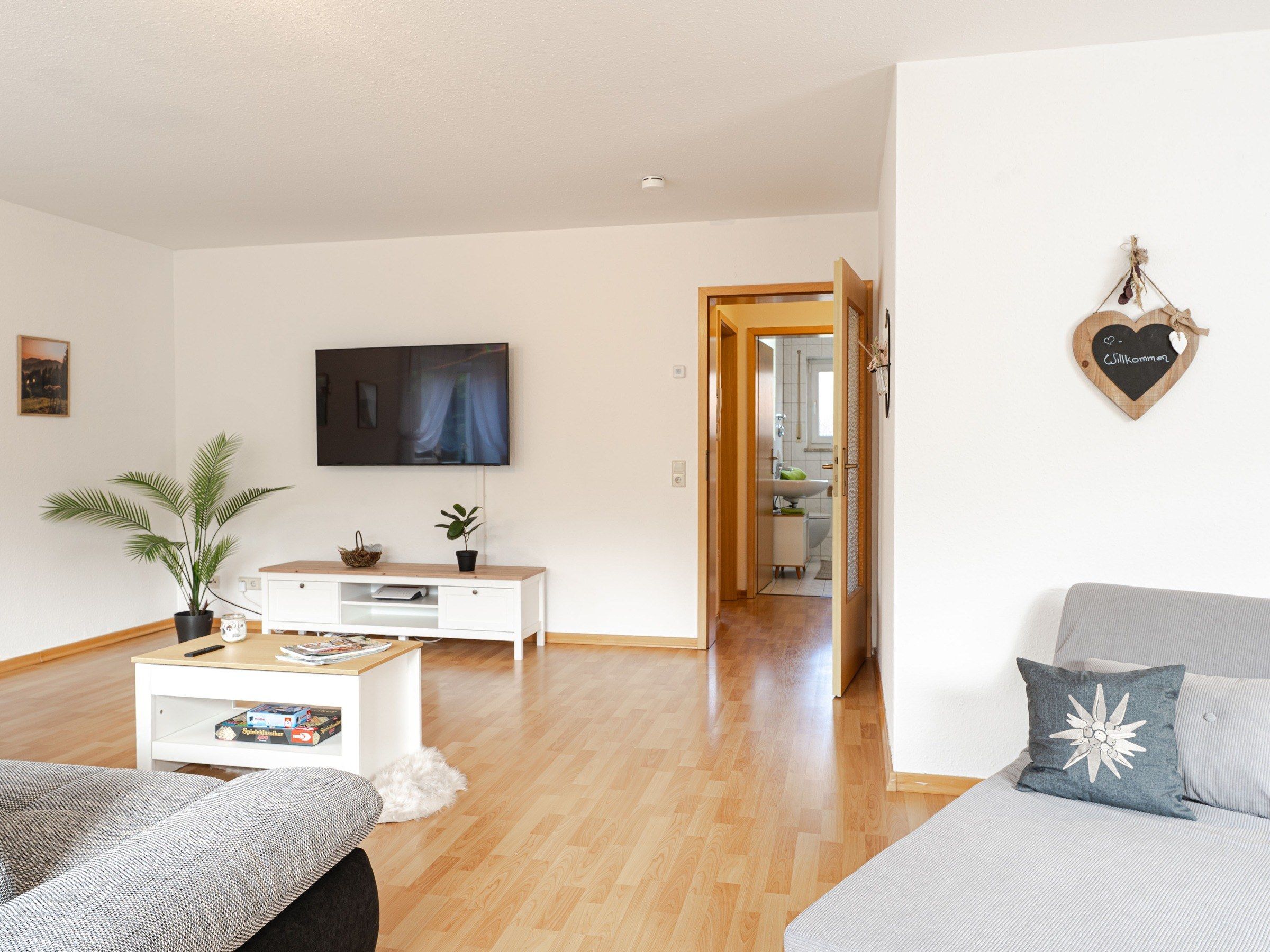 A modern living room with a flat-screen TV, a coffee table with books, a sofa, and a decorative heart on the wall.