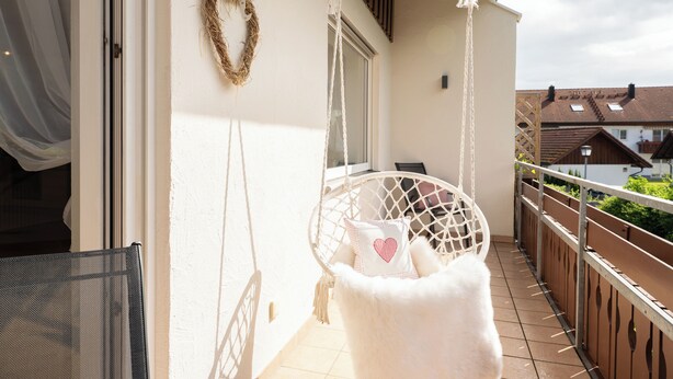 Un balcon avec une chaise blanche, une guirlande suspendue et un objet blanc et moelleux.