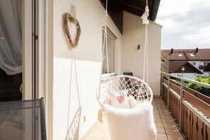 Een balkon met een witte stoel, een hangende krans en een zacht, wit voorwerp.