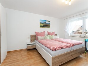 A bedroom with a bed, a nightstand, a window with curtains, and a wall-mounted picture.