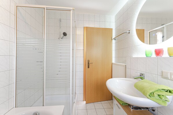 A bathroom with a glass shower enclosure, a wooden door, a white sink with a green towel, and a mirror above the sink. - Light-flooded vacation apartment Felix - your Allgäu dream in a quiet idyll (Weitnau)