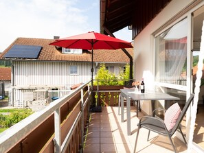 A balcony with a table, chairs, a red umbrella, and a bottle of wine. - Light-flooded vacation apartment Felix - your Allgäu dream in a quiet idyll (Weitnau)