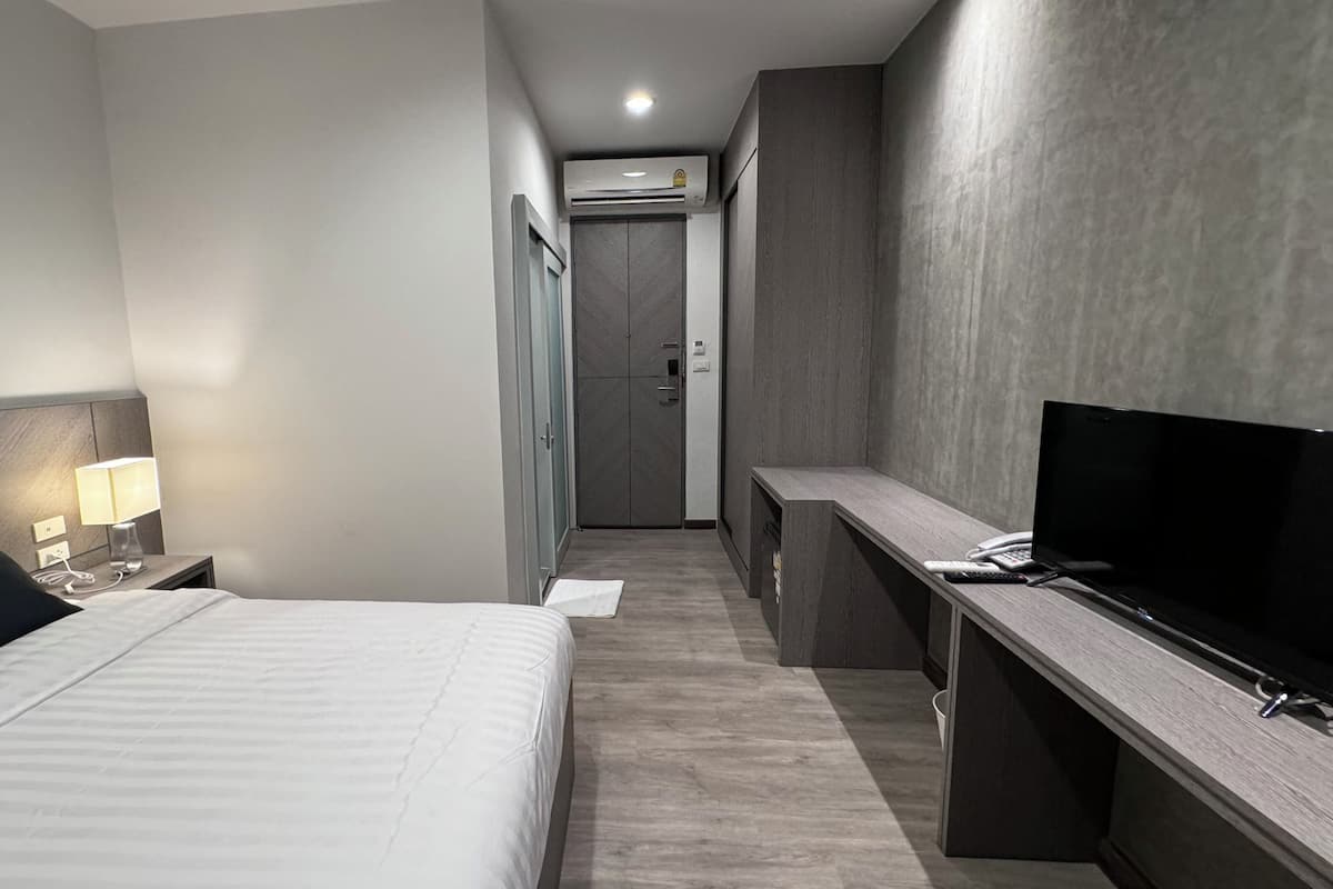 A hotel room with a bed, bedside table, lamp, TV, desk, and wardrobe.