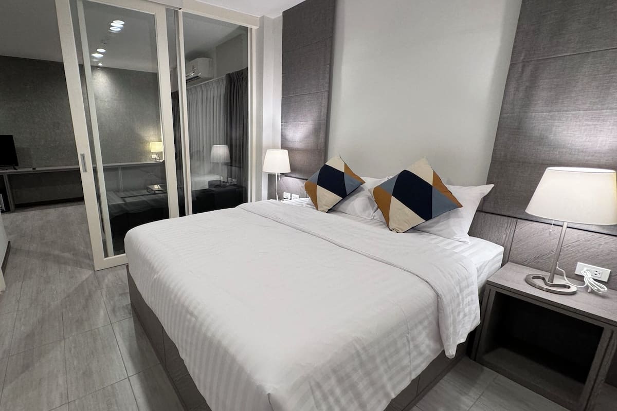A modern hotel room with a large bed, a bedside table with a lamp, and a sliding door leading to a bathroom.