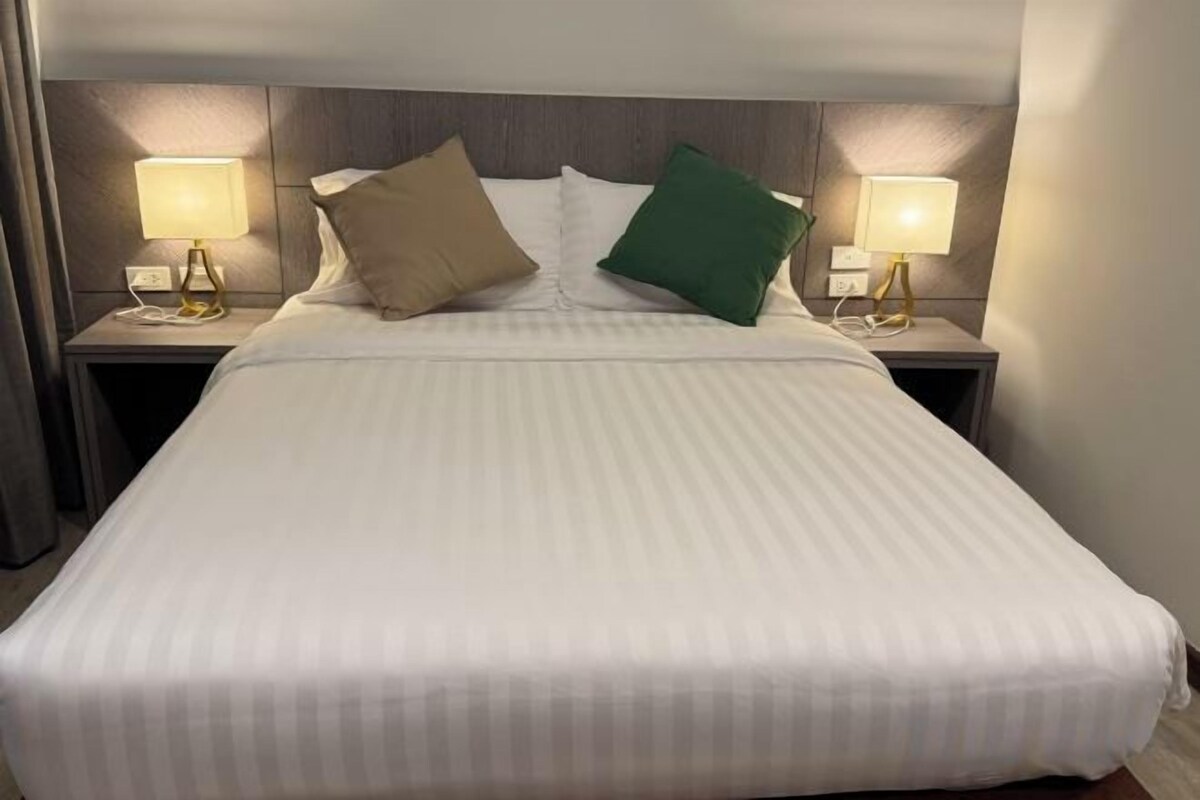 A hotel room with a large bed, two bedside lamps, and a headboard.