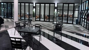 A modern indoor dining area with black and white tiled flooring, black metal tables and chairs, and large windows allowing natural light. - The Kite Hotel Bangkok (Bangkok)
