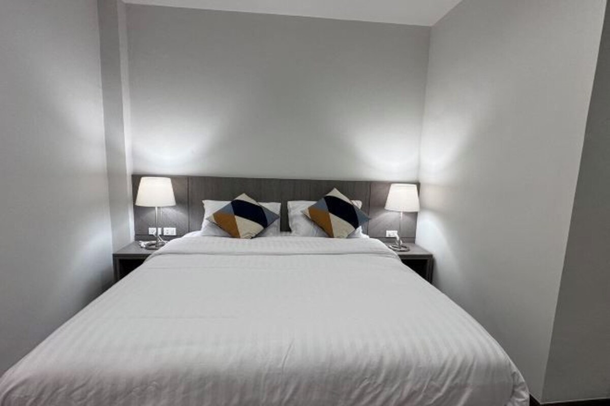 Una cama bien hecha con sábanas blancas y dos almohadones decorativos, flanqueada por dos mesitas de noche con lámparas.