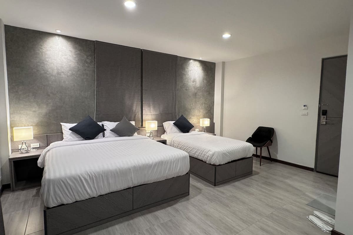 A modern hotel room with two beds, bedside lamps, a chair, and a wardrobe.