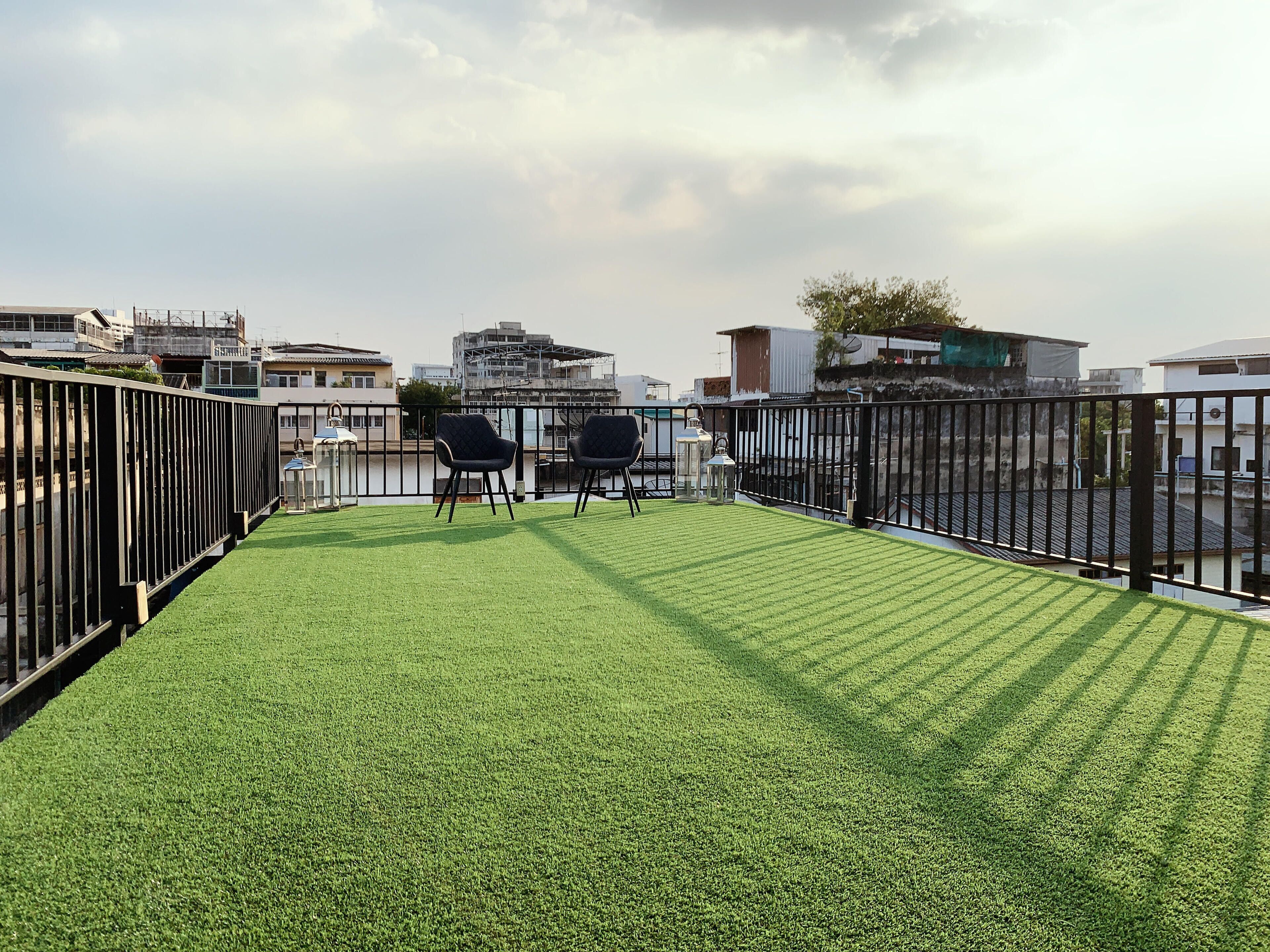 A rooftop terrace with artificial grass, two black chairs, and a metal railing.