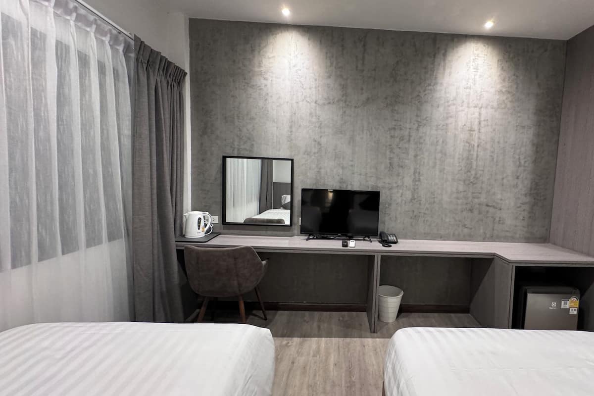 A hotel room with a bed, a desk with a computer, a chair, a small trash bin, and a wardrobe.