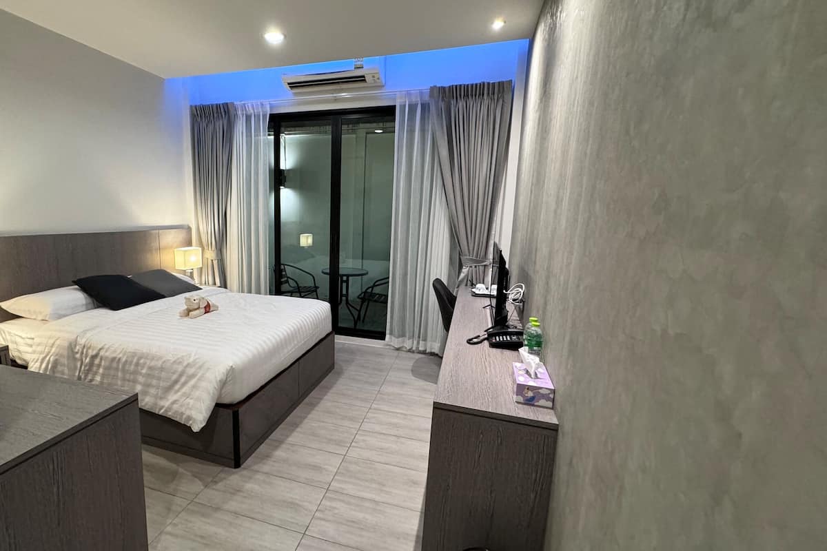 A modern hotel room with a large bed, a desk with a computer, and a balcony with curtains.