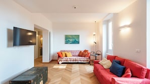 Un salon avec un canapé, un divan rouge, une malle verte et un tableau accroché au mur.