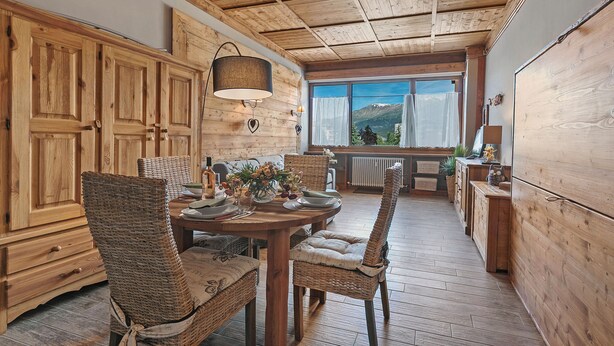 A wooden interior with a dining table, wicker chairs, and a view of mountains. - Studio Charming Sportinia Town Center (Sauze d'Oulx)