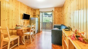 A wooden interior with a dining area, a TV mounted on the wall, and a view through a door. - Appartamento la Cerbiatta 5min Jouvenceaux Lift (Sauze d'Oulx)