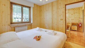 A wooden-paneled room with a bed, a window with heart-shaped curtains, a radiator, and a fire extinguisher. - Appartamento la Cerbiatta 5min Jouvenceaux Lift (Sauze d'Oulx)