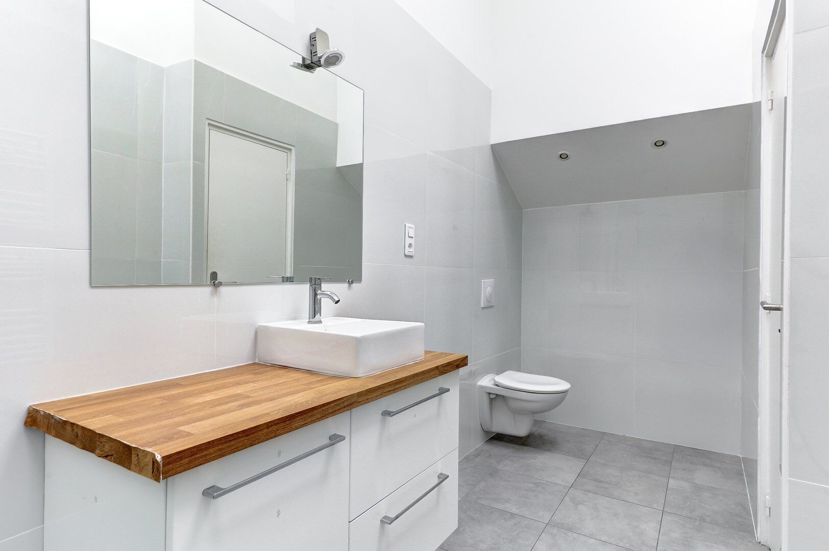 Une salle de bain moderne avec un plan de toilette en bois, un lavabo blanc, un miroir et des toilettes.