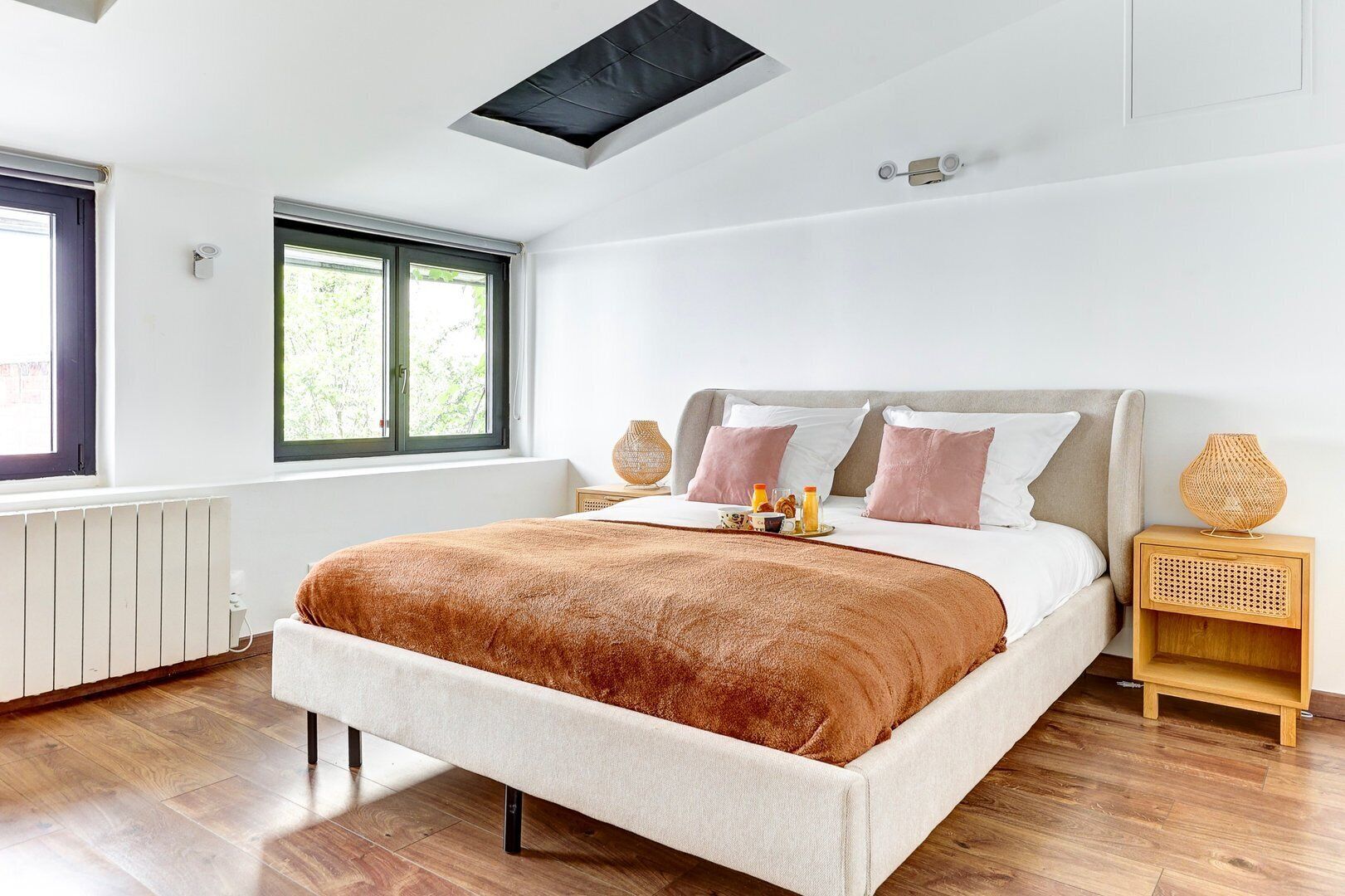 A modern bedroom with a bed, a skylight, a window, a bedside table, and a radiator.