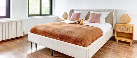 A modern bedroom with a bed, a skylight, a window, a bedside table, and a radiator.