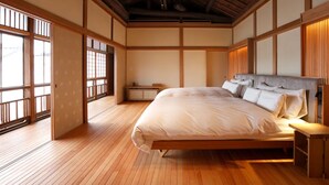 A traditional Japanese-style bedroom with tatami flooring, a low platform bed, sliding doors, and a view of the outside through large windows. - mameya (Sasayama)