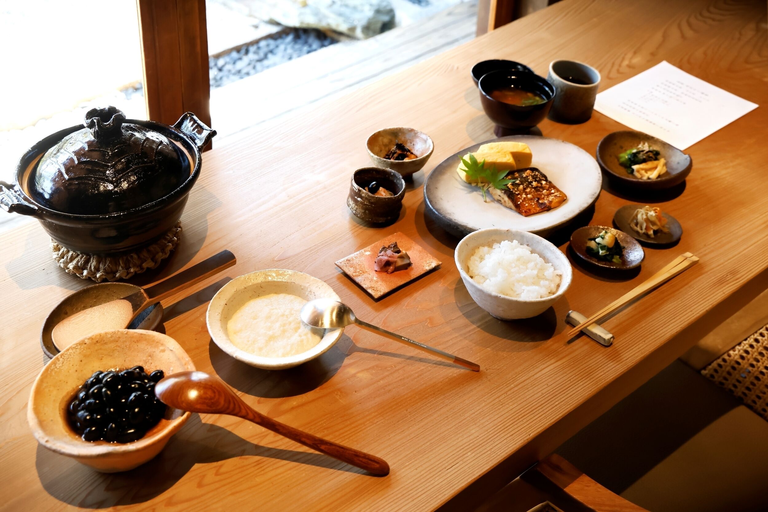 A wooden table with various dishes, including a pot, bowls of rice, and small plates with food.