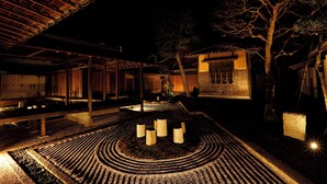 A traditional Japanese-style building at night with a wooden exterior, a tiled courtyard, and a large tree in the background. - mameya (Sasayama)