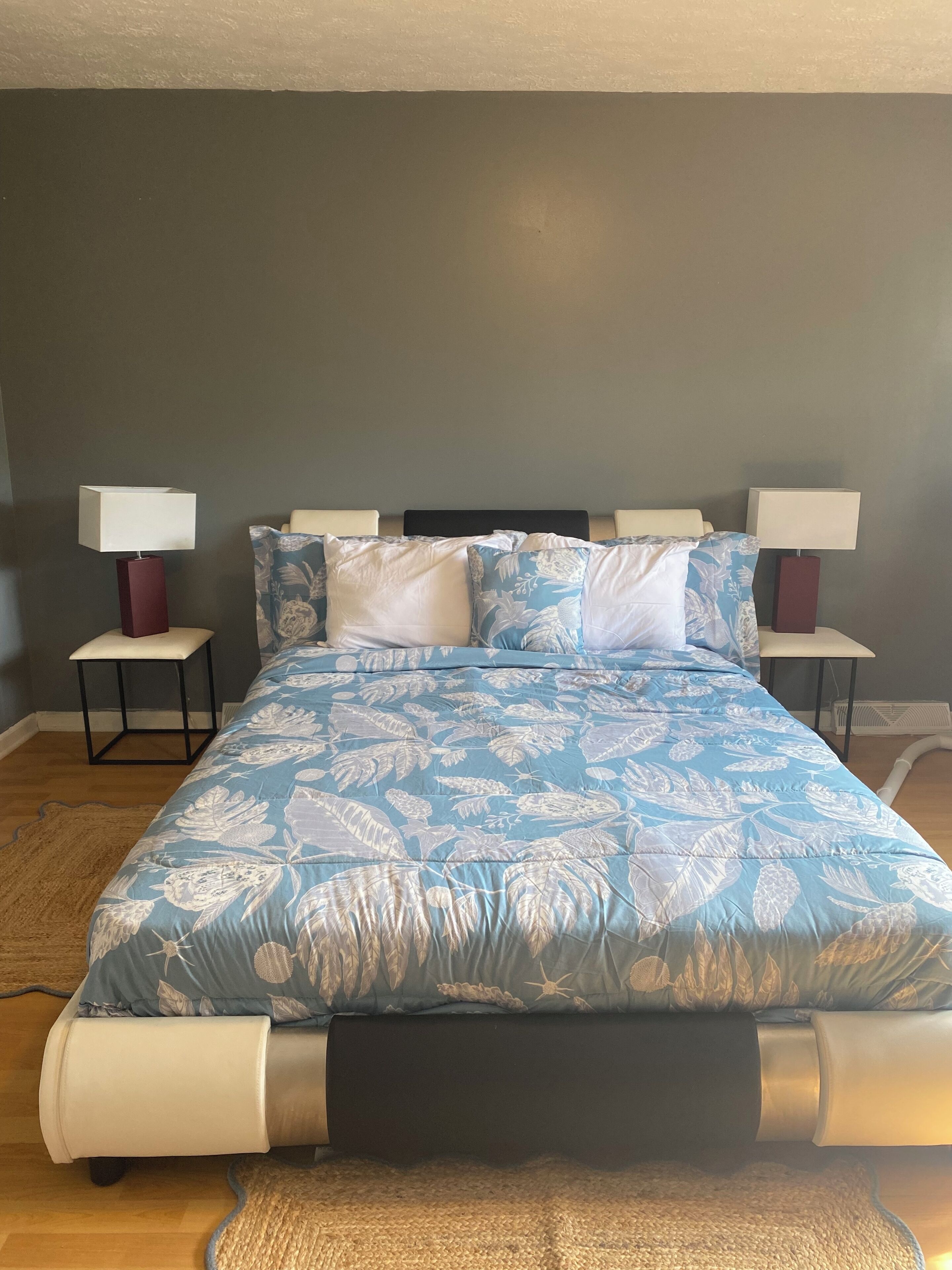 A bedroom with a bed, two bedside tables with lamps, a dark headboard, and a patterned bedspread.