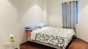 Un dormitorio con una cama, una mesita de noche con un florero y una ventana con cortinas.