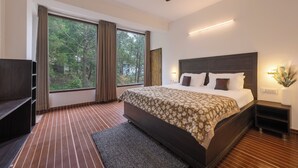 A modern hotel room with a large bed, a ceiling fan, a TV, and a view of trees through the window. - The Chalet Homestay (Kasauli)